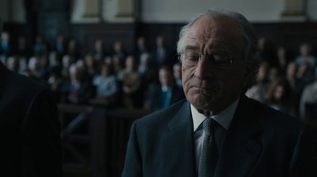 Movie still from “The Wizard of Lies” (2017), directed by Barry Levinson – An older man in a suit and tie in front of a group of people; Close Up shot, Low angle
