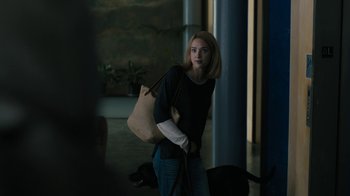 Movie still from “The Wizard of Lies” (2017), directed by Barry Levinson – A woman holding a purse while standing next to a dog; Medium shot, Over the shoulder angle