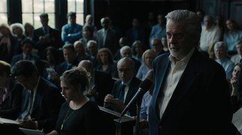 Movie still from “The Wizard of Lies” (2017), directed by Barry Levinson – An older man is speaking at a public event; Medium shot, Low angle
