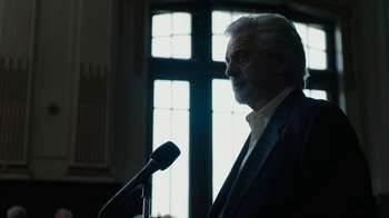 Movie still from “The Wizard of Lies” (2017), directed by Barry Levinson – An older man is speaking into a microphone in front of a window; Close Up shot, Low angle