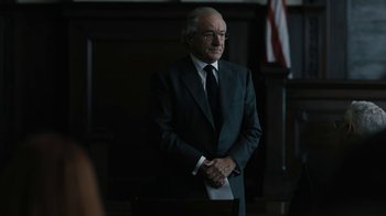 Movie still from “The Wizard of Lies” (2017), directed by Barry Levinson – An older man in a suit standing in front of an american flag; Medium shot, Over the shoulder angle