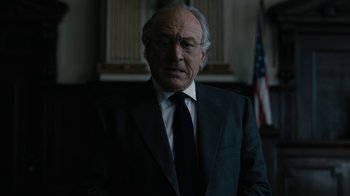 Movie still from “The Wizard of Lies” (2017), directed by Barry Levinson – An older man in a suit and tie in front of an american flag; Close Up shot, Low angle