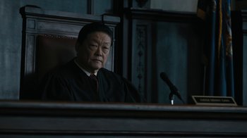 Movie still from “The Wizard of Lies” (2017), directed by Barry Levinson – A man sitting in front of a microphone in a courtroom; Close Up shot, Over the shoulder angle