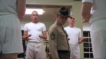 Movie still from “Full Metal Jacket” (1987), directed by Stanley Kubrick – A group of men standing in a room with a man in a uniform; Medium shot, Low angle