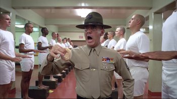 Movie still from “Full Metal Jacket” (1987), directed by Stanley Kubrick – A man in uniform holding a donut in front of a group of men; Medium shot, Low angle