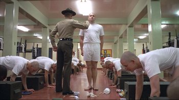 Movie still from “Full Metal Jacket” (1987), directed by Stanley Kubrick – A man in white shirt standing next to a man in white shirt; Wide shot, Low angle