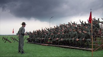Movie still from “Full Metal Jacket” (1987), directed by Stanley Kubrick – A group of men sitting in front of a man in a uniform; Wide shot, High angle
