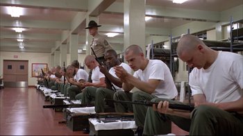 Movie still from “Full Metal Jacket” (1987), directed by Stanley Kubrick – A group of men sitting next to each other holding guns; Wide shot, Low angle
