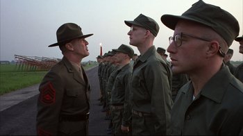 Movie still from “Full Metal Jacket” (1987), directed by Stanley Kubrick – A group of men standing next to each other on a road; Medium shot, Over the shoulder angle