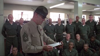 Movie still from “Full Metal Jacket” (1987), directed by Stanley Kubrick – A man in a military uniform is holding a book; Medium shot, Low angle