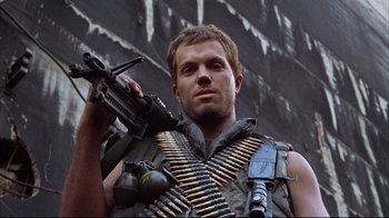 Movie still from “Full Metal Jacket” (1987), directed by Stanley Kubrick – A man holding a gun while standing in front of a building; Close Up shot, Low angle