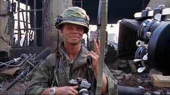 Movie still from “Full Metal Jacket” (1987), directed by Stanley Kubrick – A man holding a rifle and a camera in his hand; Medium shot, Low angle