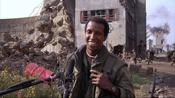 Movie still from “Full Metal Jacket” (1987), directed by Stanley Kubrick – A man standing next to a motorcycle in front of a building; Medium shot, Low angle