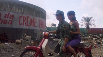 Movie still from “Full Metal Jacket” (1987), directed by Stanley Kubrick – A man and a woman on a moped in front of an advertisement; Wide shot, Low angle