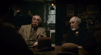 Movie still from “The Wolfman” (2010), directed by Joe Johnston – Two men sitting at a wooden table in a room; Medium shot, Over the shoulder angle
