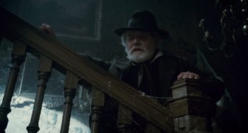 Movie still from “The Wolfman” (2010), directed by Joe Johnston – An old man wearing a hat leaning on a railing; Medium shot, Low angle