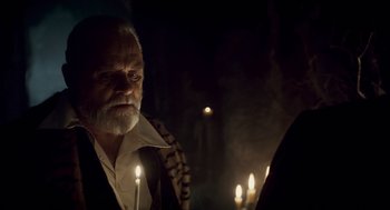 Movie still from “The Wolfman” (2010), directed by Joe Johnston – An old man with a beard is looking at candles in the dark; Close Up shot, Over the shoulder angle
