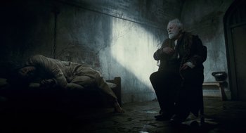 Movie still from “The Wolfman” (2010), directed by Joe Johnston – An old man sitting on the ground next to a bed; Wide shot, High angle