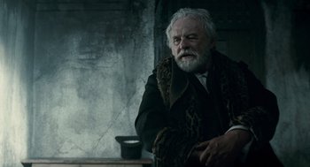 Movie still from “The Wolfman” (2010), directed by Joe Johnston – An old man with a beard and a fur coat; Medium shot, Over the shoulder angle