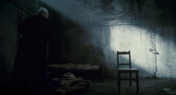 Movie still from “The Wolfman” (2010), directed by Joe Johnston – A chair and bed in a room with a brick wall; Wide shot, High angle