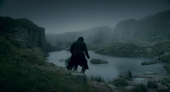 Movie still from “The Wolfman” (2010), directed by Joe Johnston – A man in a long coat walking on a hill near a lake; Extreme Wide shot, High angle
