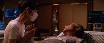 Movie still from “The Wolverine” (2013), directed by James Mangold – An older man laying on a bed with a nurse standing next to him; Medium shot, Over the shoulder angle