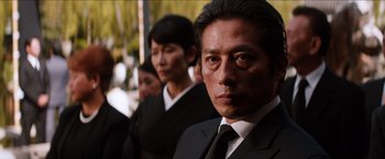Movie still from “The Wolverine” (2013), directed by James Mangold – A man in a suit and tie standing next to other people; Close Up shot, Low angle