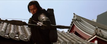 Movie still from “The Wolverine” (2013), directed by James Mangold – A man holding a bow and arrow on top of a building; Medium shot, Low angle