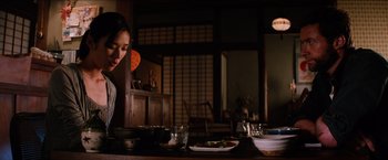 Movie still from “The Wolverine” (2013), directed by James Mangold – A woman sitting at a table with a plate of food; Medium shot, Low angle