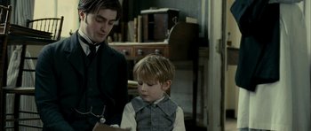 Movie still from “The Woman in Black” (2012), directed by James Watkins – A man and a boy in a room with books; Medium shot, Over the shoulder angle