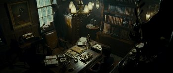 Movie still from “The Woman in Black” (2012), directed by James Watkins – A man sitting at a desk in a room with many books; Wide shot, High angle