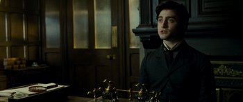 Movie still from “The Woman in Black” (2012), directed by James Watkins – A man sitting in front of a table with a bunch of brass pipes; Close Up shot, Over the shoulder angle