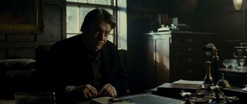 Movie still from “The Woman in Black” (2012), directed by James Watkins – A man sitting at a table writing on a piece of paper; Medium shot, Over the shoulder angle
