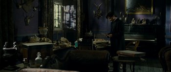Movie still from “The Woman in Black” (2012), directed by James Watkins – A man standing in a living room looking at a phone; Wide shot, High angle