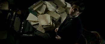 Movie still from “The Woman in Black” (2012), directed by James Watkins – A man standing in front of a pile of papers; Medium shot, High angle