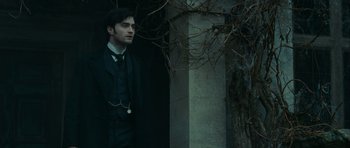 Movie still from “The Woman in Black” (2012), directed by James Watkins – A man standing next to a tree in front of a building; Medium shot, Over the shoulder angle