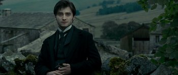 Movie still from “The Woman in Black” (2012), directed by James Watkins – A man in a suit and tie standing in front of a stone wall; Medium shot, Over the shoulder angle