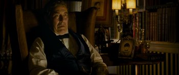 Movie still from “The Woman in Black” (2012), directed by James Watkins – An older man sitting in a chair wearing a vest and tie; Close Up shot, Over the shoulder angle