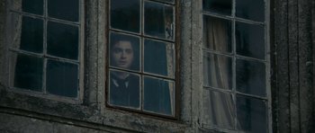 Movie still from “The Woman in Black” (2012), directed by James Watkins – A man looking out of a window in a building; Medium shot, Over the shoulder angle