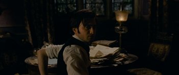 Movie still from “The Woman in Black” (2012), directed by James Watkins – A man sitting in front of papers in a dark room; Medium shot, Over the shoulder angle