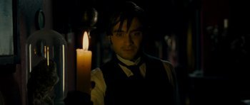 Movie still from “The Woman in Black” (2012), directed by James Watkins – A man standing in front of a lit candle in the dark; Medium shot, Over the shoulder angle