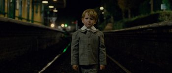 Movie still from “The Woman in Black” (2012), directed by James Watkins – A boy in a suit stands on the train tracks at night; Medium shot, High angle