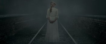 Movie still from “The Woman in Black” (2012), directed by James Watkins – A woman in a white dress standing on train tracks in the fog; Medium shot, High angle
