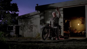 Movie still from “The World's Fastest Indian” (2005), directed by Roger Donaldson – An older man sitting on a motorcycle outside a building; Wide shot, Low angle