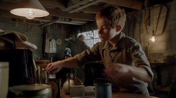 Movie still from “The World's Fastest Indian” (2005), directed by Roger Donaldson – A young boy is pouring something into a cup; Medium shot, Low angle