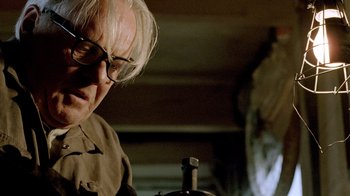 Movie still from “The World's Fastest Indian” (2005), directed by Roger Donaldson – An older man wearing glasses looking down at something; Close Up shot, Low angle