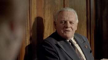 Movie still from “The World's Fastest Indian” (2005), directed by Roger Donaldson – An older man wearing a suit and tie in front of a wooden wall; Close Up shot, Over the shoulder angle