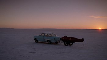 Movie still from “The World's Fastest Indian” (2005), directed by Roger Donaldson – An old car is towing a boat in the middle of the desert; Extreme Wide shot, High angle