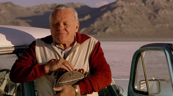 Movie still from “The World's Fastest Indian” (2005), directed by Roger Donaldson – An older man holding a shoe on the side of a boat in front of mountains; Close Up shot, Low angle