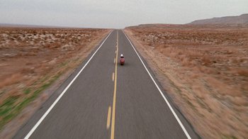 Movie still from “The World's Fastest Indian” (2005), directed by Roger Donaldson – A person riding a motorcycle down the middle of a road; Extreme Wide shot, High angle